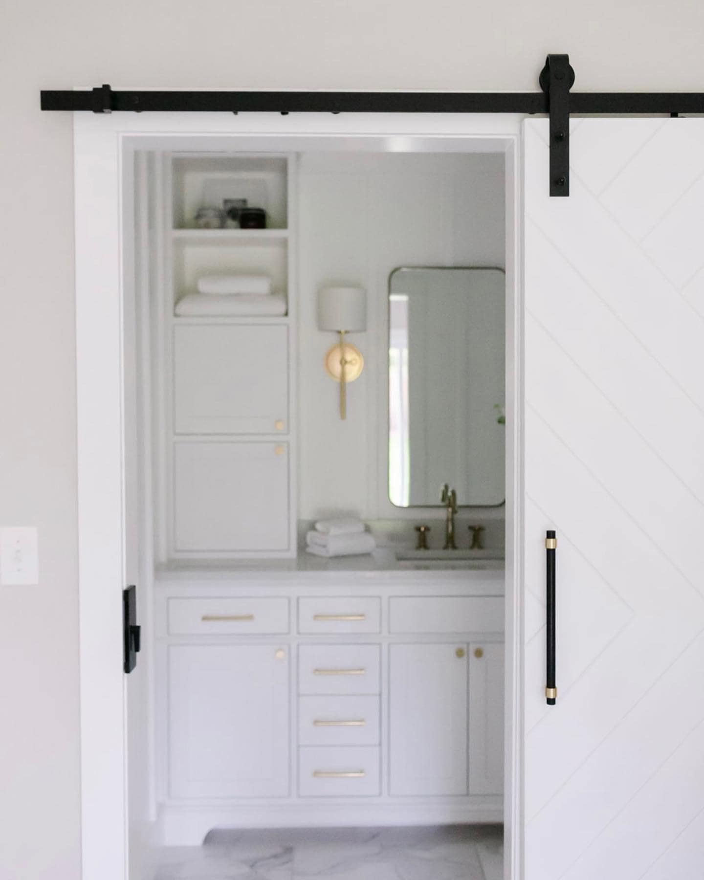 White bathroom sink and cupboards seen through barn-style door